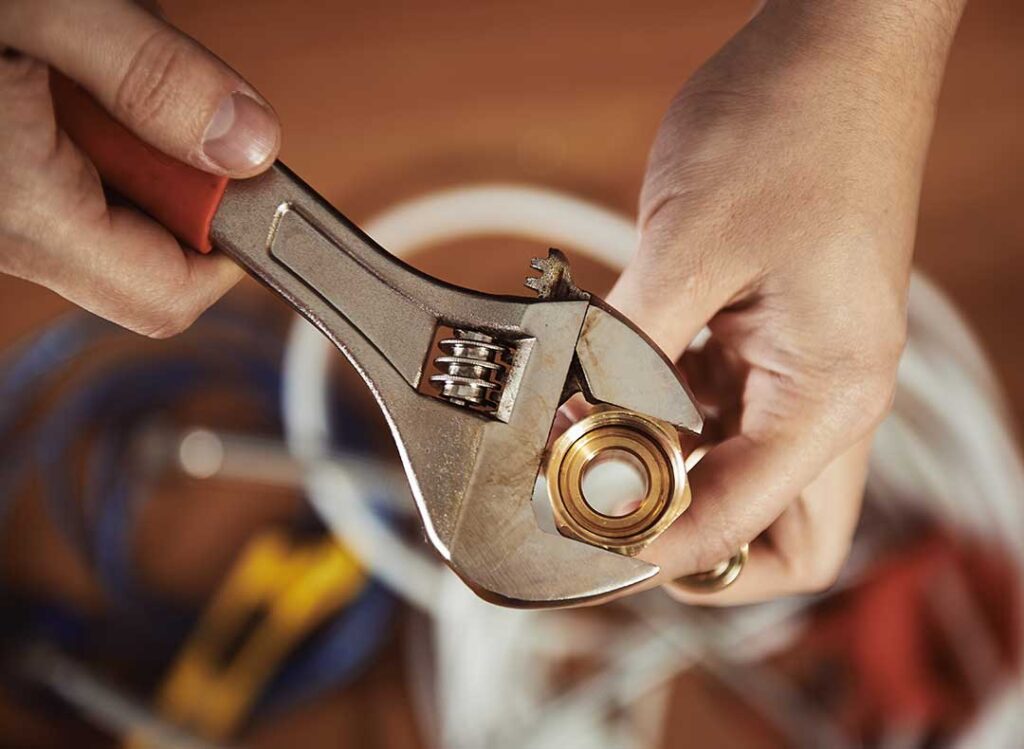 Person with gloves and wrench replacing a toilet flapper inside a typical home bathroom.