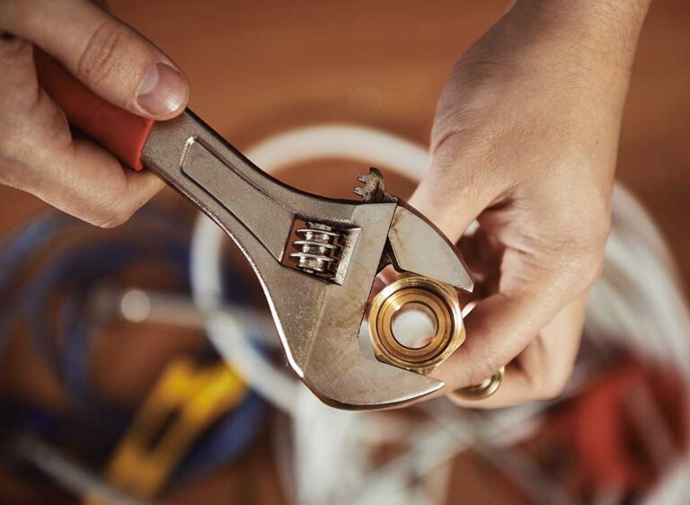 Person with gloves and wrench replacing a toilet flapper inside a typical home bathroom.
